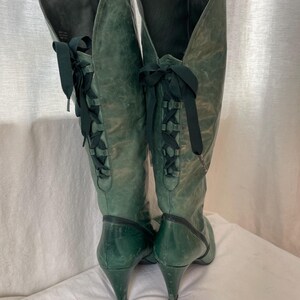May include: A pair of green leather knee-high boots with black laces up the back. The boots have a pointed toe and a high heel.