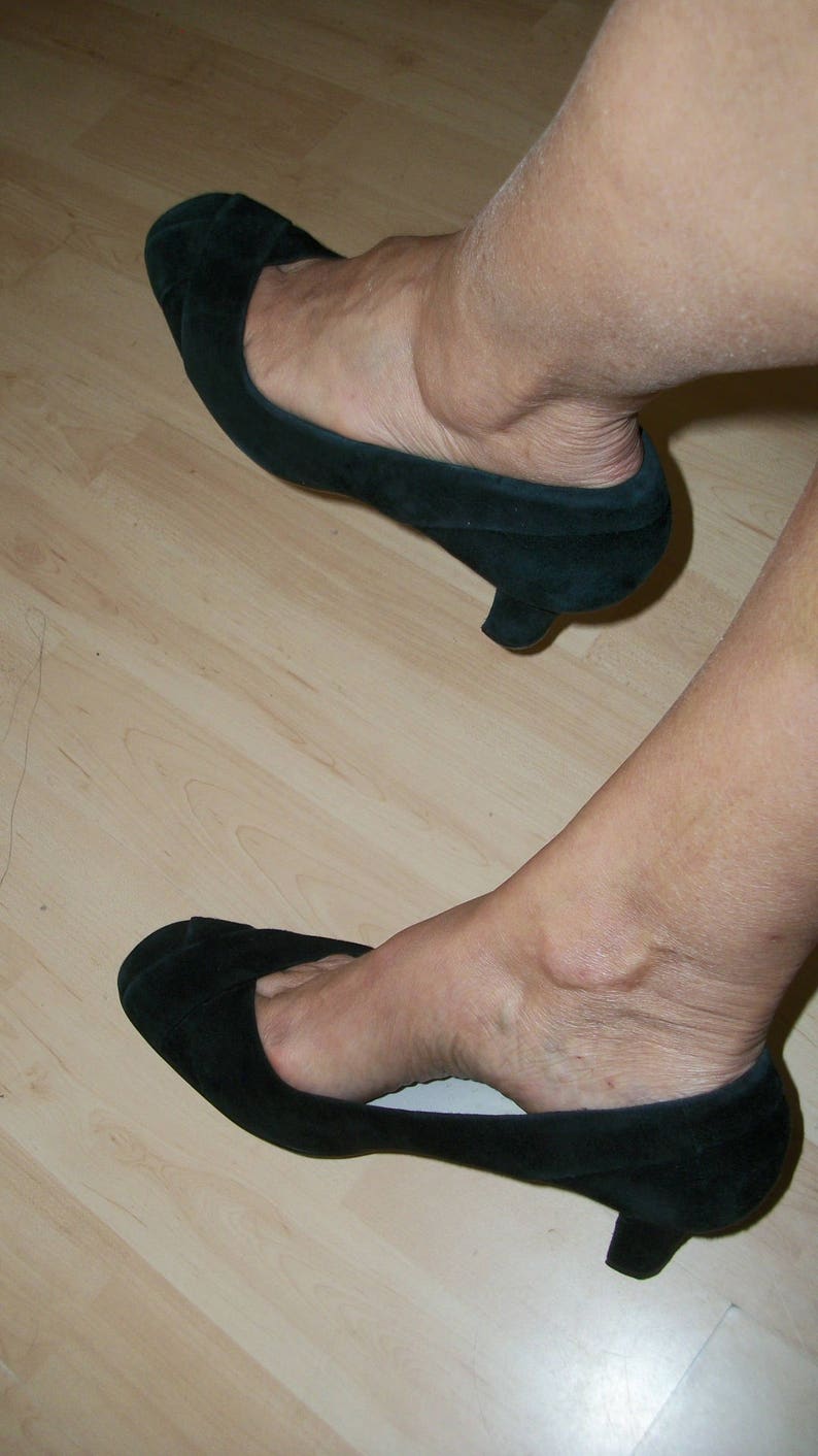 Peut inclure: Une paire de chaussures &agrave; talons en daim noir avec une pointe pointue. Les chaussures sont sur un sol en bois.