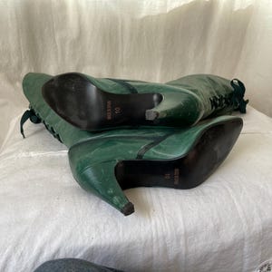 May include: A pair of green leather knee-high boots with lace-up fronts and stiletto heels. The boots are size 10 and have the brand name "Nice n Easy" printed on the soles.