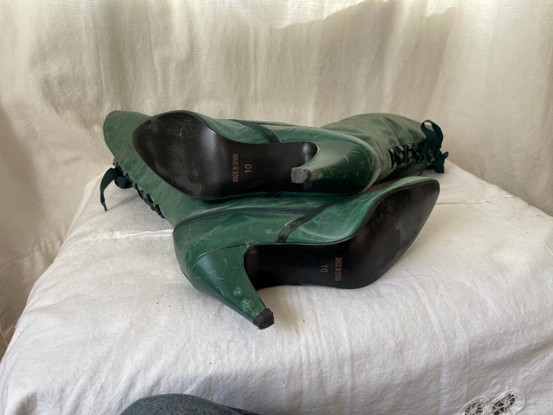 May include: A pair of green leather knee-high boots with lace-up fronts and stiletto heels. The boots are size 10 and have the brand name "Nice n Easy" printed on the soles.