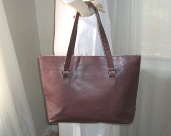 May include: A brown leather tote bag with two long straps. The bag has a simple design and is made of a high-quality leather.