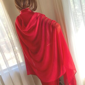 May include: A bright red sheer shawl draped over a person's shoulders. The shawl is made of a lightweight fabric and has a flowing, elegant look.