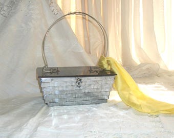 May include: A silver and white woven clutch purse with a silver handle and a yellow satin scarf attached.