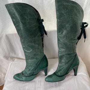 May include: A pair of green leather knee-high boots with lace-up detailing and a heel.