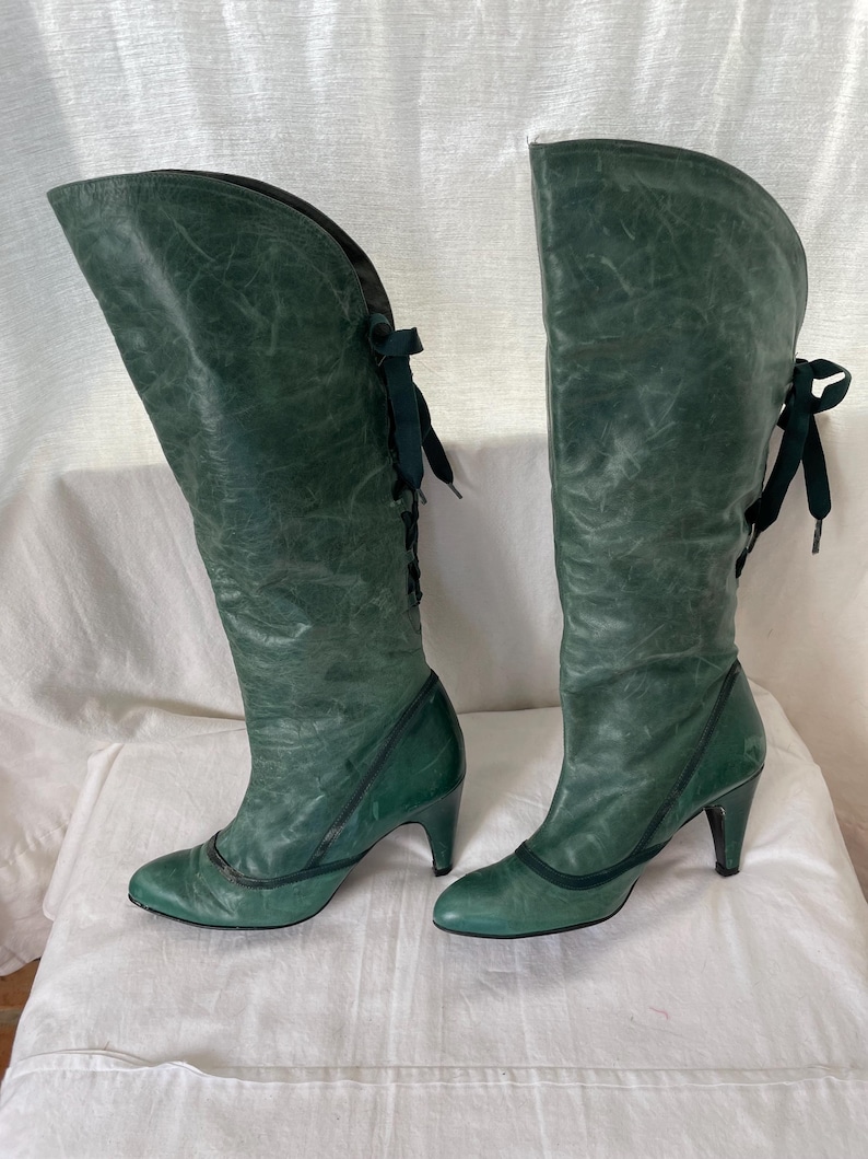 May include: A pair of green leather knee-high boots with lace-up detailing and a heel.