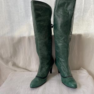 May include: A pair of green leather knee-high boots with a pointed toe and a small heel.