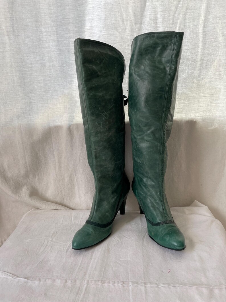 May include: A pair of green leather knee-high boots with a pointed toe and a small heel.