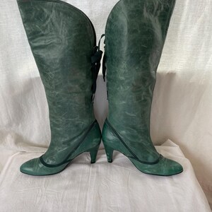 May include: A pair of green leather knee-high boots with a lace-up back and a small heel.