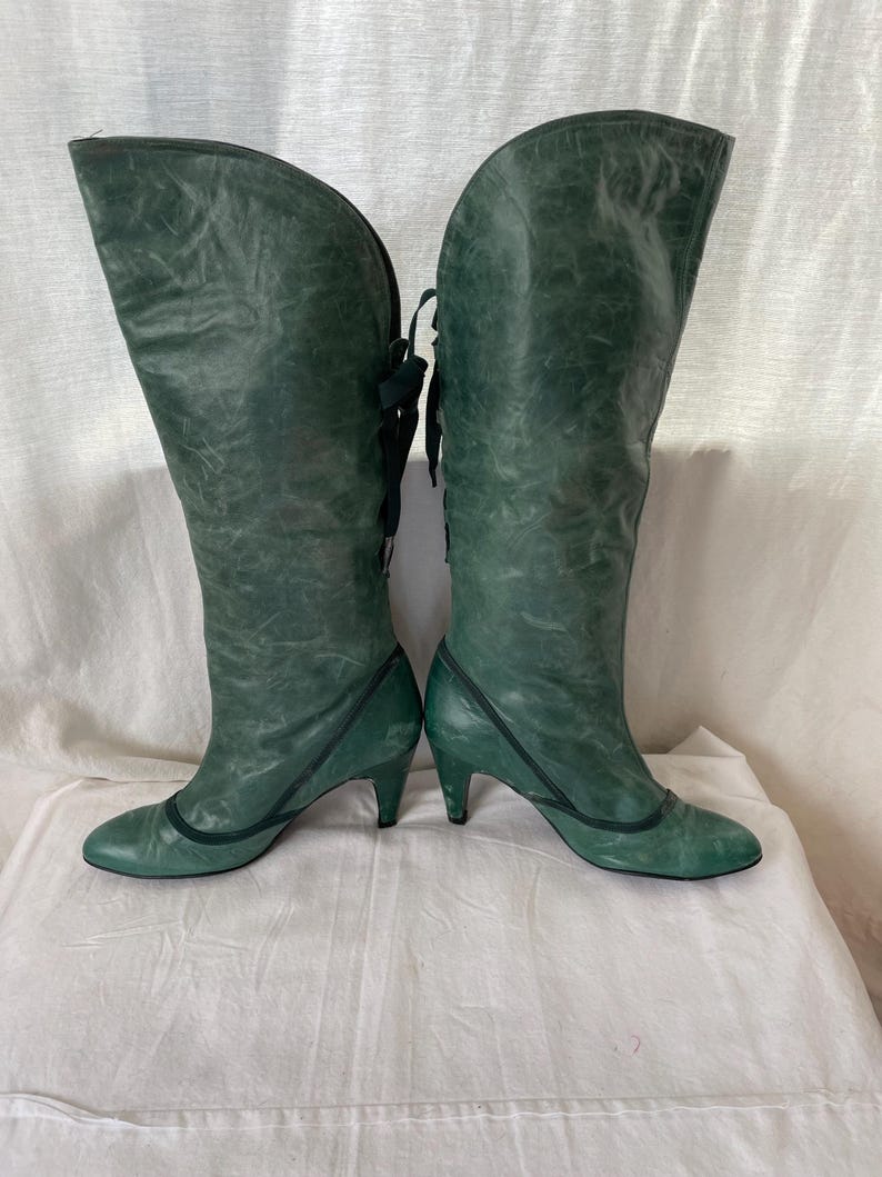May include: A pair of green leather knee-high boots with a lace-up back and a small heel.