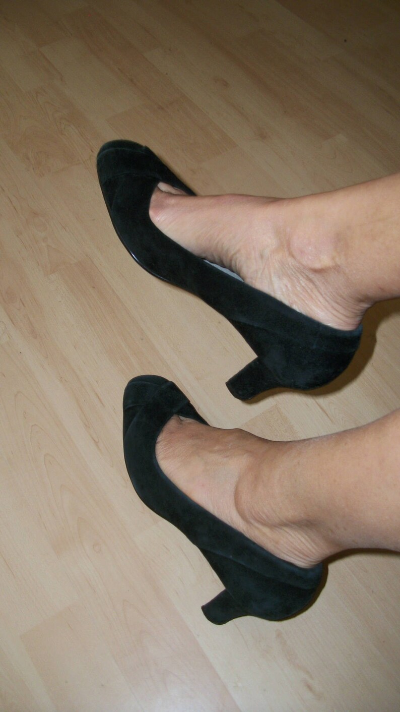 Peut inclure: Une paire de chaussures &agrave; talons en daim noir avec bout pointu. Les chaussures sont port&eacute;es sur un sol en bois.