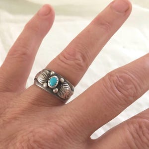 May include: A silver ring with a turquoise stone set in the center, surrounded by leaf-shaped designs.