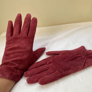 May include: A pair of red suede gloves. The gloves are soft and have a textured surface.