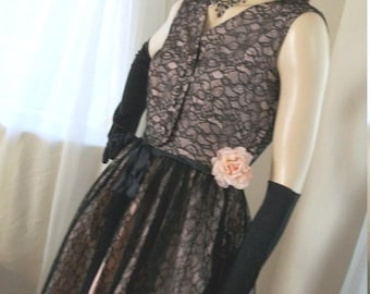 May include: A black and pink lace dress with a floral accent. The dress has a fitted bodice and a full skirt. The model is wearing black gloves.