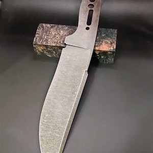 Könnte beinhalten: Eine blanke, unfertige Klingenform mit einer strukturierten Oberfläche und einem Griff mit drei Löchern. Die Klinge ist aus Metall und hat eine leicht gebogene Form.