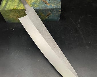 May include: A long, thin, silver knife with a sharp point and a textured blade. The knife is lying on a dark surface.