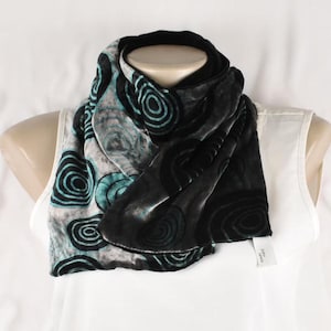 May include: A black and teal velvet scarf with a swirling pattern. The scarf is folded and displayed on a white mannequin.