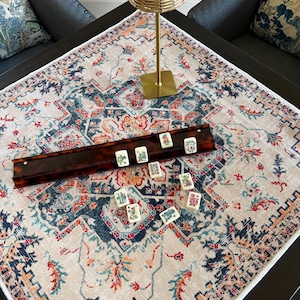 May include: A square tablecloth with a cream base and a multi-colored floral and geometric pattern in shades of navy blue, orange, and teal. A long, dark brown tortoiseshell-patterned mahjong tile rack holds several tiles with colorful designs.