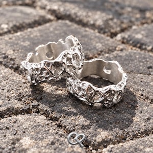 May include: Two silver-toned rings featuring an irregular, porous, and textured surface reminiscent of organic coral or molten metal. The bands have a polished finish with visible circular cutouts along the inner edges and a small logo symbol.