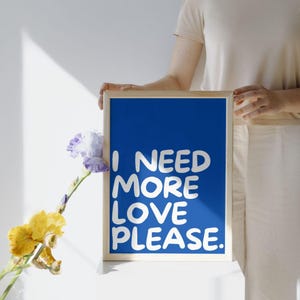 Peut inclure: Une affiche encadrée bleue avec du texte blanc qui dit "J'ai besoin de plus d'amour s'il vous plaît."