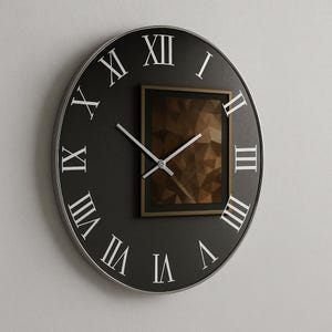 May include: A round black wall clock with white Roman numerals and silver hands. A rectangular frame with a geometric design is centered on the clock face. The clock has a silver-coloured metal rim.