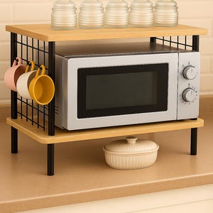 Puede incluir: Un horno microondas sobre una estantería de madera de dos niveles con detalles de metal negro. La estantería superior contiene tarros de cristal, la estantería inferior tiene un plato de cerámica y tazas de colores. La estantería mide 60 cm de ancho.