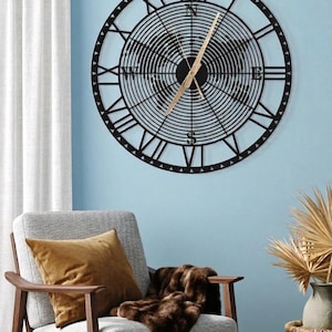 May include: A large, circular wall clock featuring a black metal frame with Roman numerals and a concentric line pattern. A stylized world map is integrated into the center, with gold-colored hands and cardinal direction letters N, S, E, and W.