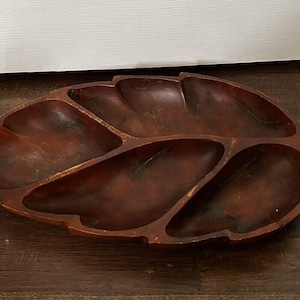May include: A dark brown wooden serving dish shaped like a leaf with five sections. The dish is made from a single piece of wood and has a natural, rustic finish.