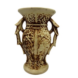 May include: Cream-colored ceramic vase with brown decorative patterns. The vase features two handles and a flared rim. The design includes floral and scrollwork motifs, adding a vintage aesthetic. The vase is suitable for displaying flowers or as a decorative piece.