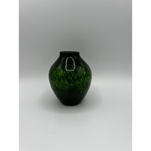 Könnte beinhalten: Eine dunkelgrüne Glasvase mit einem gesprenkelten Muster. Die Vase hat einen abgerundeten Körper und einen schmalen Hals. Das Glas hat eine glänzende Oberfläche und eine dunkelgrüne Farbe mit helleren grünen Sprenkeln.