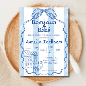 May include: Blue and white baby shower invitation with the words "Bonjour Bébé" in script. The invitation includes details for Amelia Jackson's baby shower, with a cafe illustration and RSVP information.