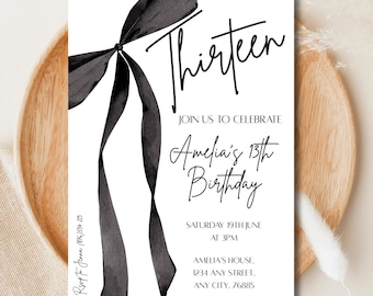 May include: A white birthday invitation featuring a black ribbon and the word "Thirteen" in cursive. The invitation text reads "Join us to celebrate Amelia's 13th Birthday" with event details. The card is on a wooden plate.