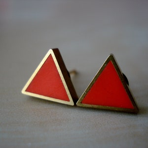 May include: A pair of triangle-shaped earrings with a gold metal frame and a bright orange centre.