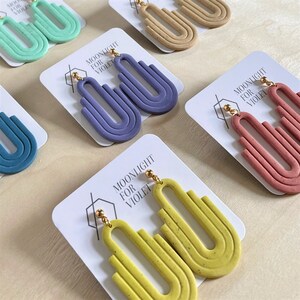 Può includere: Un set di sei paia di orecchini fatti a mano. Ogni paio presenta un colore e un design unici. Gli orecchini sono realizzati in argilla polimerica e hanno una texture punteggiata. Gli orecchini hanno la forma di una serie di archi. Gli orecchini sono esposti su carte bianche con il testo "Moonlight for Violet".