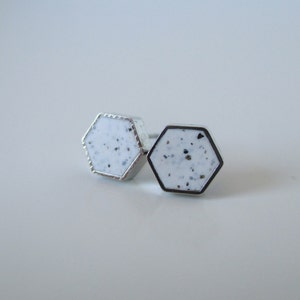 Puede incluir: Un par de pendientes de botón hexagonales de plata con un diseño blanco moteado.