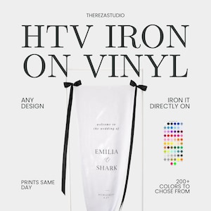 Op de afbeelding: Wit HTV-opstrijkvinyl met zwarte tekst "HTV IRON ON VINYL". De afbeelding toont een trouwteken met de namen "EMILIA & SHARK". Het bord wordt weergegeven op een witte metalen standaard met zwarte linten. De afbeelding toont ook een kleurenkaart.