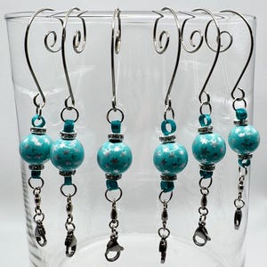 May include: Set of six teal blue and silver snowflake ornament hooks. Each hook features a teal blue bead with silver snowflake accents, a silver ribbon, and a silver chain with a lobster clasp.