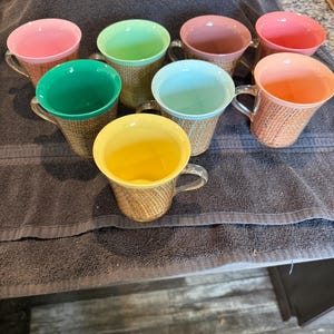 Puede incluir: Conjunto de ocho tazas coloridas con un patrón tejido. Las tazas son en tonos de rosa, verde, azul, amarillo y naranja.