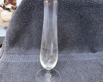 May include: A clear glass vase with a silver rim and a wide base. The vase is sitting on a gray towel.