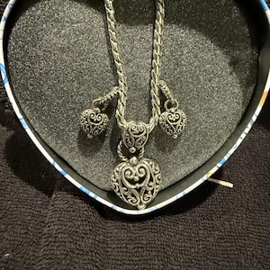 Puede incluir: Un collar de plata en forma de coraz&oacute;n con dos peque&ntilde;os colgantes en forma de coraz&oacute;n que cuelgan de la cadena. El collar est&aacute; en una caja en forma de coraz&oacute;n.