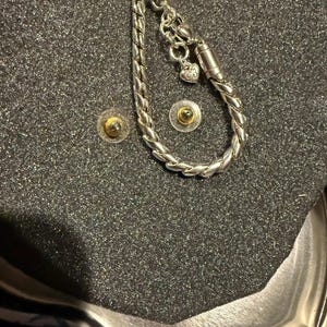 Puede incluir: Un brazalete de plata con un dije en forma de coraz&oacute;n y un cierre magn&eacute;tico. El brazalete se muestra sobre un fondo negro.