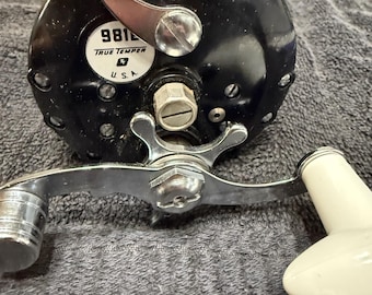 May include: A black fishing reel with a silver handle and a white knob. The reel has a label that says "9812 TRUE TEMPER U.S.A."