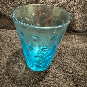 Può includere: Un bicchiere di vetro blu con un design testurizzato a forma di bolle. Il vetro è trasparente e ha un aspetto leggermente opaco.