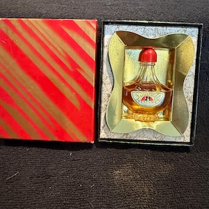 May include: A vintage perfume bottle in a gold and black box. The bottle is clear glass with a red cap and the label reads "Sagitaire Perfume".