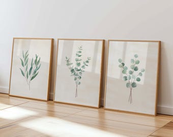 May include: Three framed botanical prints featuring watercolor eucalyptus branches. Each print has a light beige background and a natural wood frame. The eucalyptus leaves are various shades of green.