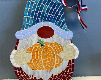 May include: A mosaic gnome holding a pumpkin. The gnome is wearing a blue hat with a white brim and a red nose. The pumpkin is orange and has a green stem. The gnome is standing on a wooden surface. The price tag says "60c".