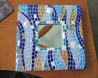 May include: A square mosaic mirror with a blue, white, and gold design. The mirror has a small rectangular mirror in the center.