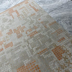 May include: A rectangular area rug with a geometric pattern. The rug features a light gray background with a repeating pattern of white and orange cross-like shapes. The rug's design is symmetrical and modern.