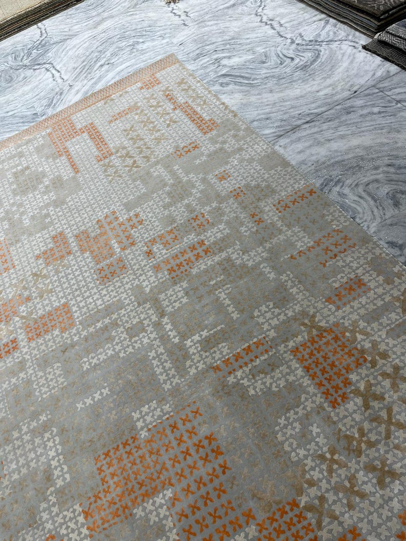 May include: A rectangular area rug with a geometric pattern. The rug features a light gray background with a repeating pattern of white and orange cross-like shapes. The rug's design is symmetrical and modern.