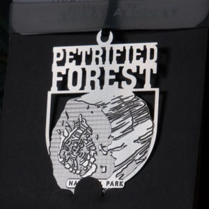 May include: A silver metal ornament with the words "Petrified Forest National Park" and a stylized image of a petrified log.