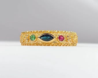 Könnte beinhalten: Ein Goldring mit einem detaillierten Design, das drei Edelsteine ​​aufweist: einen dunkelblauen, markisenförmigen Stein in der Mitte, flankiert von einem grünen und einem roten runden Stein.